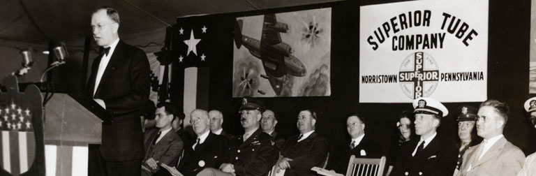Navy-Army officers at an 'E' Award ceremony at Superior Tube. Speaking at the podium is Superior’s General Manager S.L. Fabel